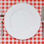 empty plate with fork and knife resting on a picnic table cloth